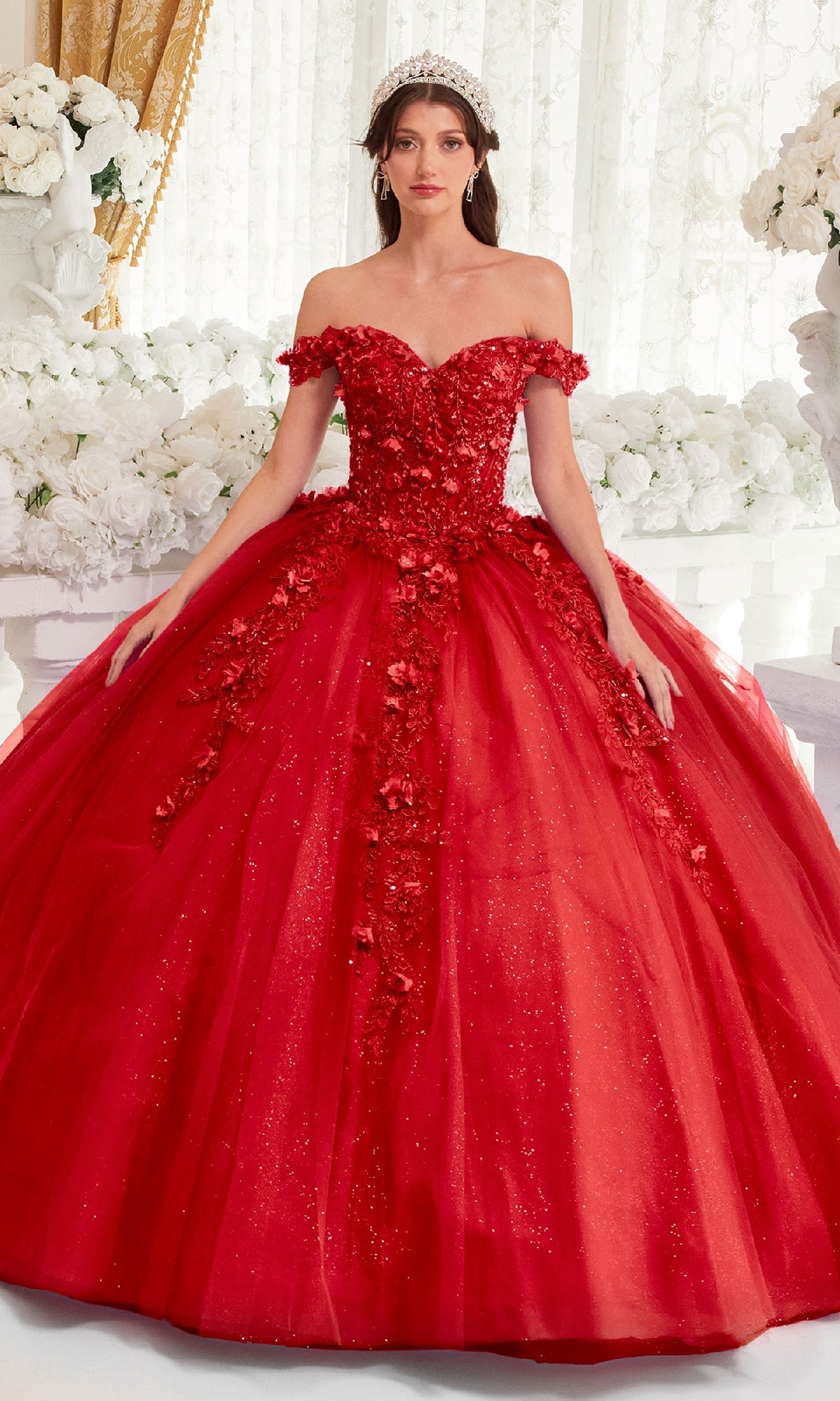 A woman stands in front of a white floral background wearing the Off-Shoulder Purple Quinceanera Dress: Ladivine 15717, featuring glitter, floral appliqués, and a full tulle skirt.